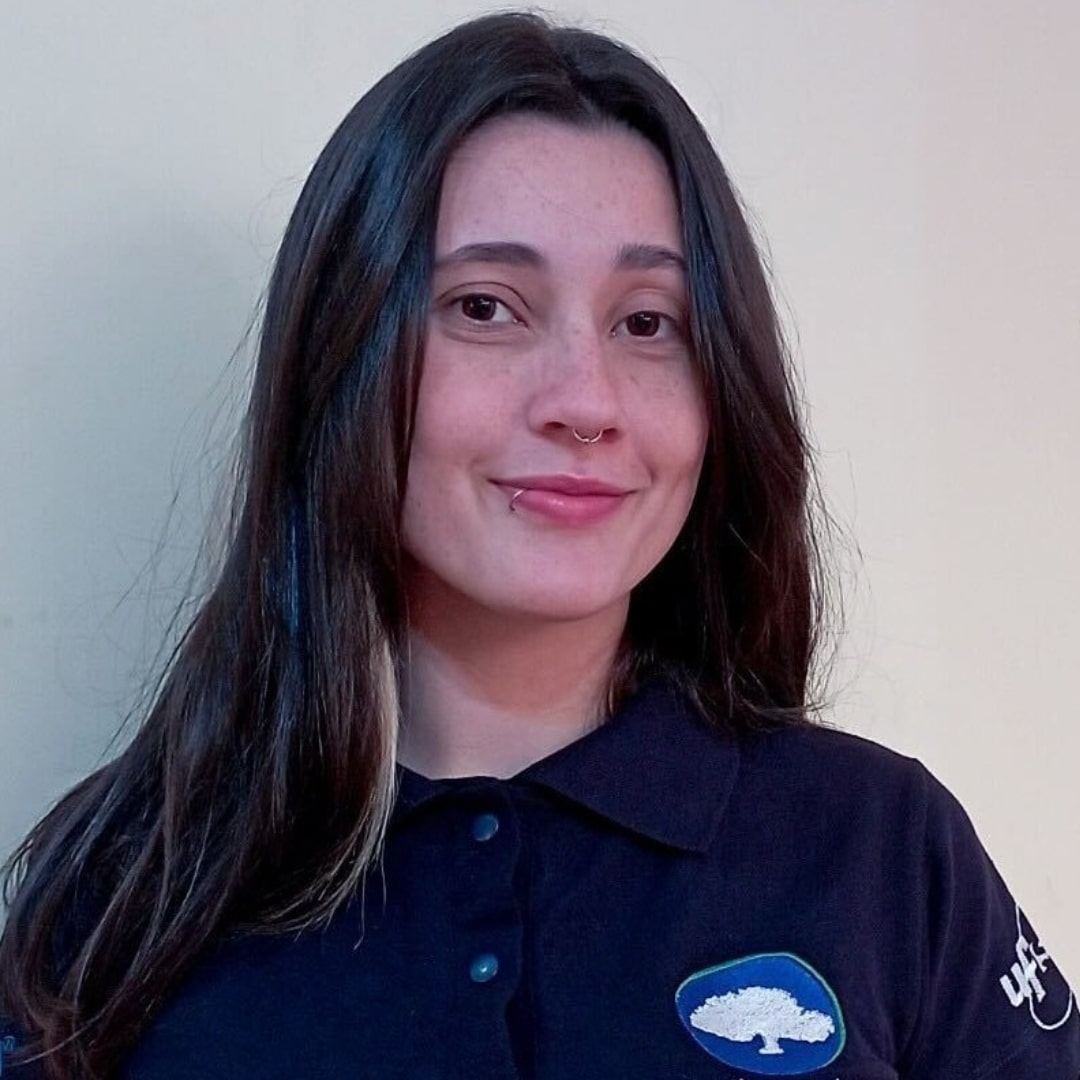 Descrição da imagem da Thamires: pele clara, olhos escuros, cabelo escuro liso, com uma mecha loira, está usando uma camisa polo azul escuro com o logo da EcoFlorestal e está sorrindo levemente pra foto